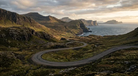 Winding coastal road curving through dramatic mountain landscape with ocean views at golden hour
