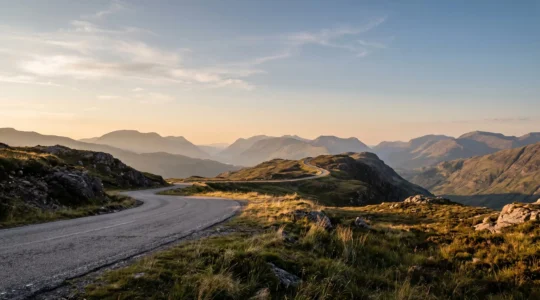 Dramatic panoramic view from a UK mountain ridge-line road at golden hour with sweeping valley vistas